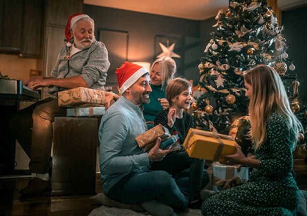 Eine fröhliche Familie sitzt vor einem festlich geschmückten Weihnachtsbaum und packt strahlend Geschenke aus.