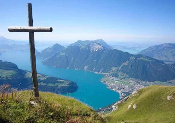 Landschaft auf einem Hügel mit Blick auf einen See, auf dem Hügel steht ein Kreuz.