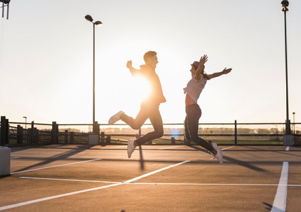 Unbekümmertes junges Paar, das bei Sonnenuntergang auf einem Parkdeck springt