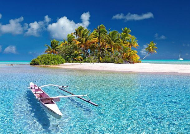 Boot auf dem himmelblauen Wasser, vor einer Insel mit Palmen.