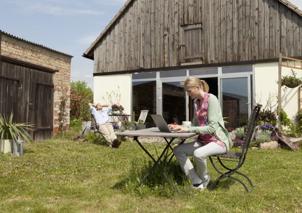 Eine Frau benutzt einen Laptop und frühstückt in ihrem Hinterhof.