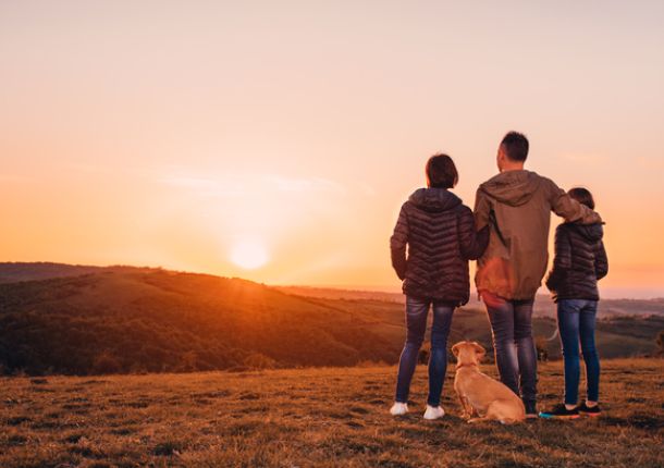 Familie mit Hund umarmt am Hügel und Blick auf den Sonnenuntergang