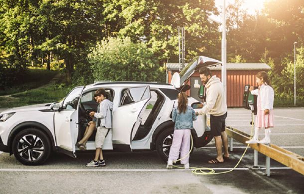 Familie auf einem Ausflug, parkend auf einem Parkplatz und beim Aufladen ihres E-Autos an einer Ladestation.