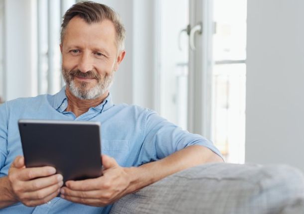 Attraktiver Mann entspannt auf einem Sofa mit einem Tablet-PC