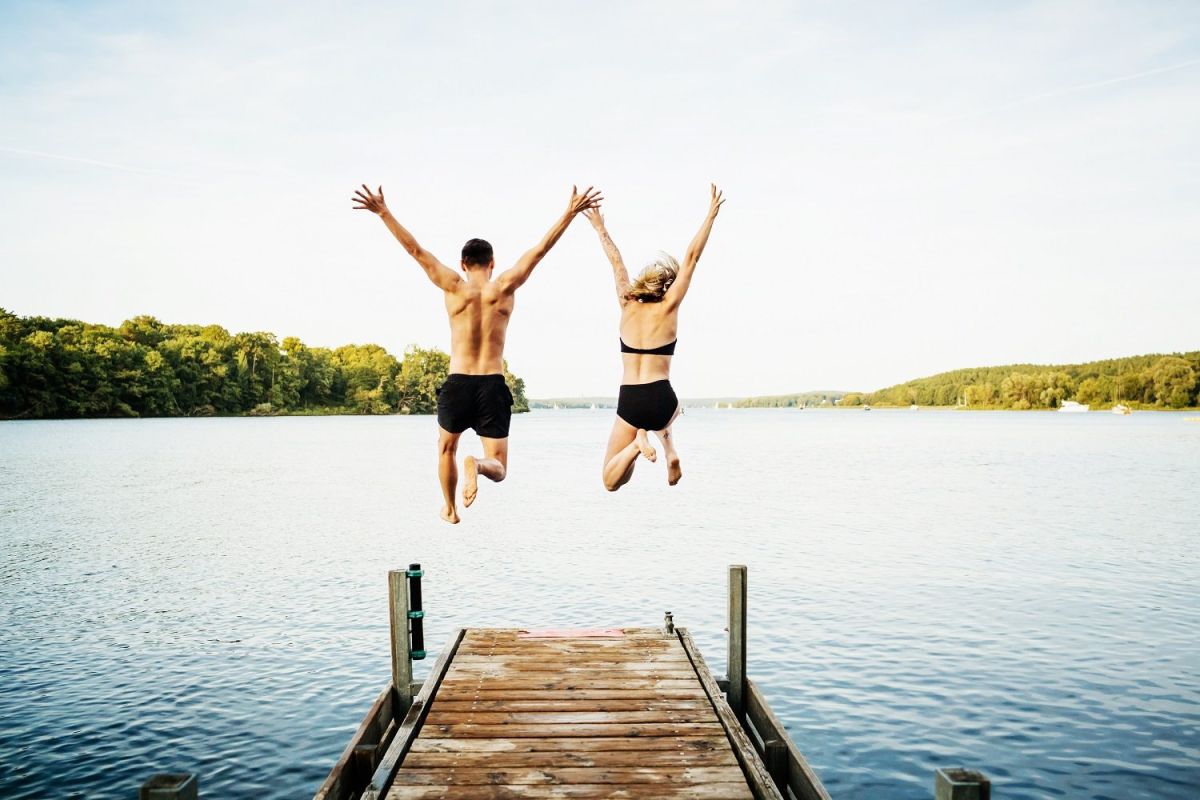 Zwei Freunde springen gemeinsam vom Steg am See