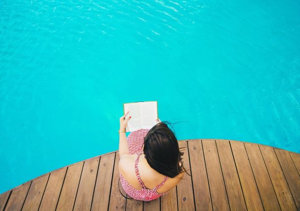 Frau am Pool beim Buch lesen