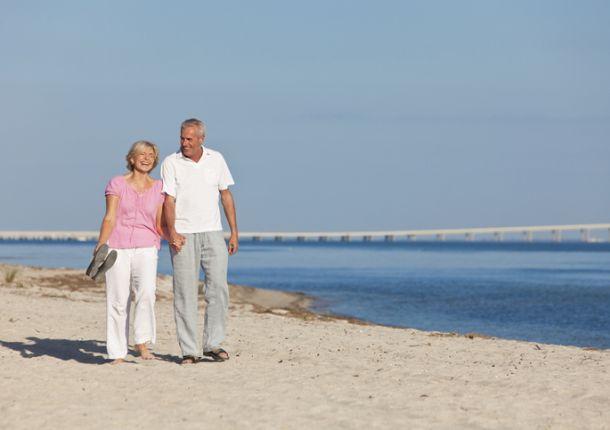 Ein glückliches Seniorenpaar geht Hand in Hand am Strand entlang