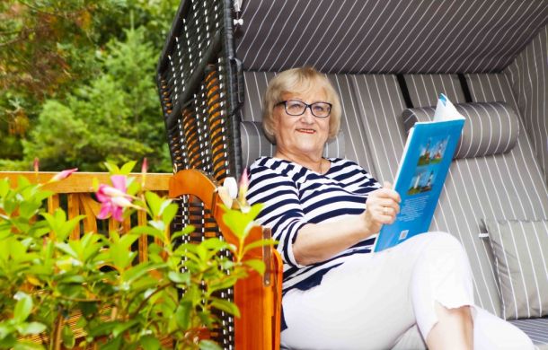 SKL Gewinnerin sitzt entspannt in ihrem Garten in einem Strandkorb und liest die Zeitung.