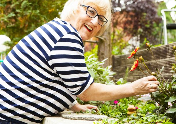 Eine ältere Frau im Garten, die sich um ihre Blumen kümmert.