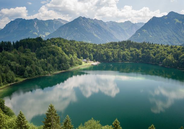 Großer See mit ruhiger Wasseroberfläche, umgeben von dichtem Wald.
