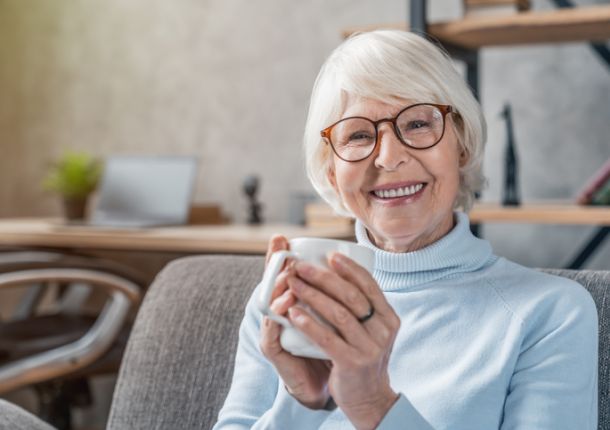 Eine ältere Frau sitzt auf der Couch mit einer Tasse in der Hand und ist eine SKL-Gewinnerin.