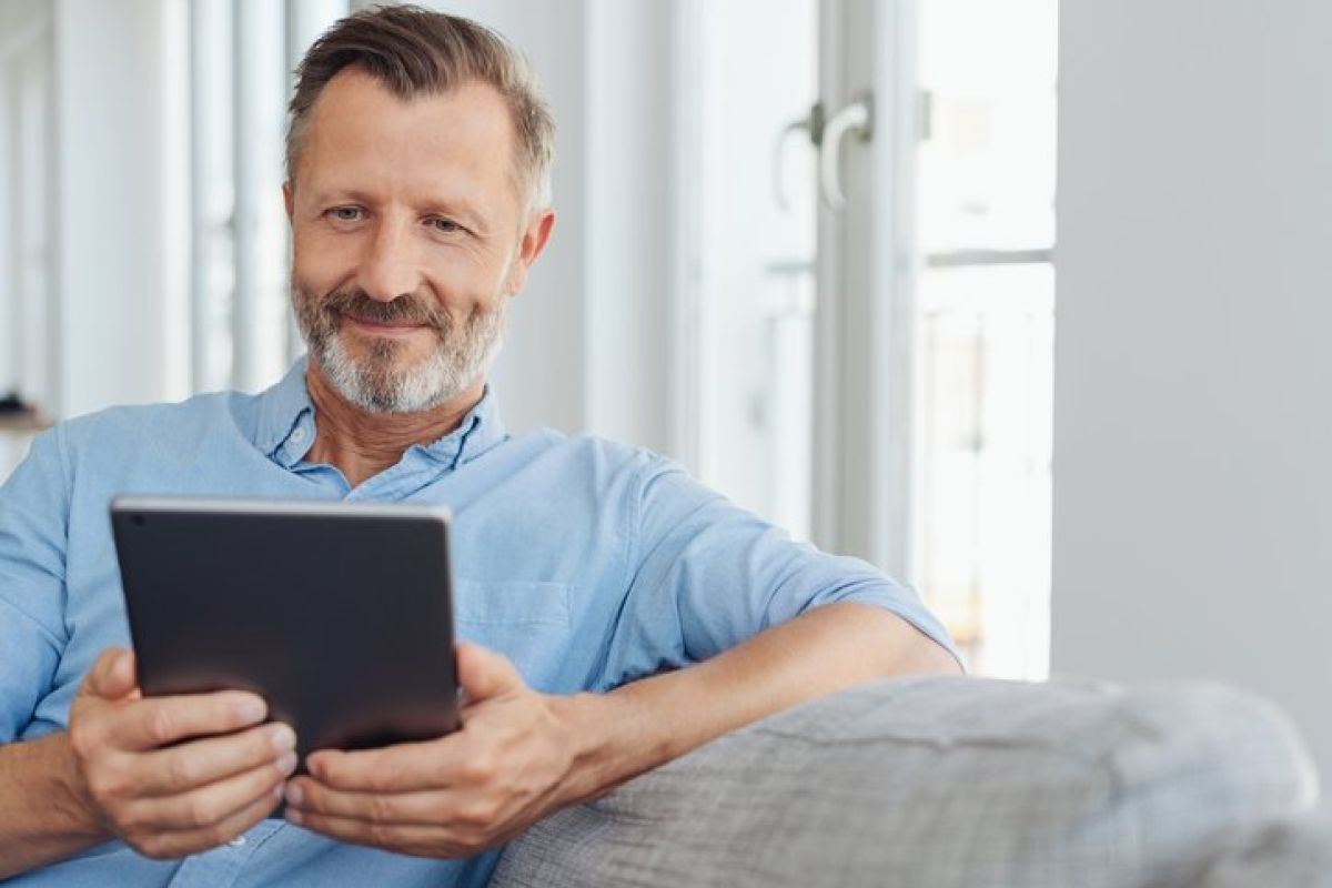 Attraktiver Mann entspannt auf einem Sofa mit einem Tablet-PC