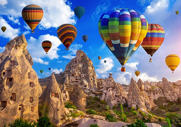 Mehrere bunte Heißluftballons steigen in den Himmel, umgeben von weißen Wolken und strahlendem Sonnenschein.