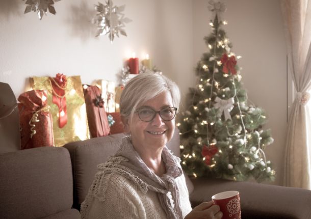 Glückliche Gloeckle Gewinnerin sitzt mit einer Tasse in der Hand auf der Couch, während im Hintergrund ein Weihnachtsbaum steht.