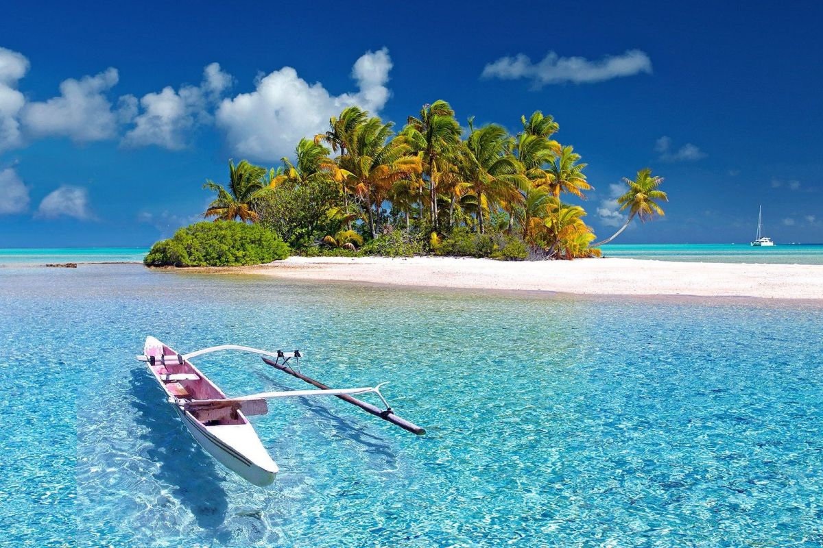 Boot auf dem himmelblauen Wasser, vor einer Insel mit Palmen.