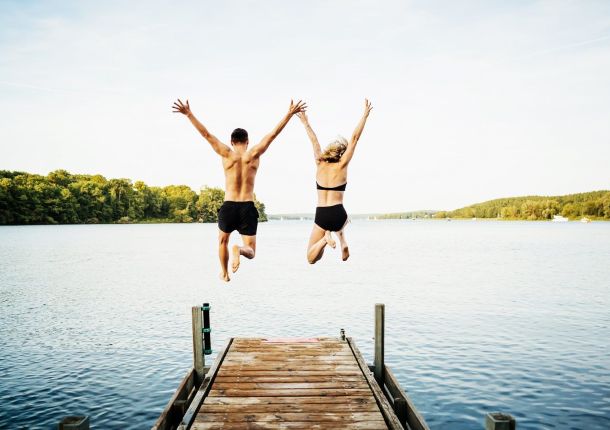 Zwei Freunde springen gemeinsam vom Steg am See