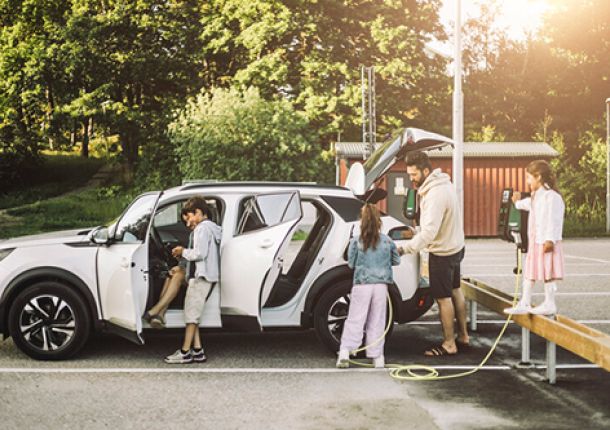 Familie auf einem Ausflug, parkend auf einem Parkplatz und beim Aufladen ihres E-Autos an einer Ladestation.