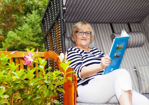 SKL Gewinnerin sitzt entspannt in ihrem Garten in einem Strandkorb und liest die Zeitung.