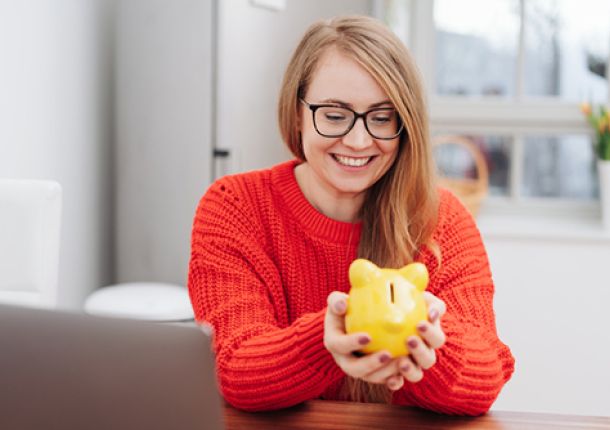 Eine blonde Frau mit einem Sparschwein in der Hand.