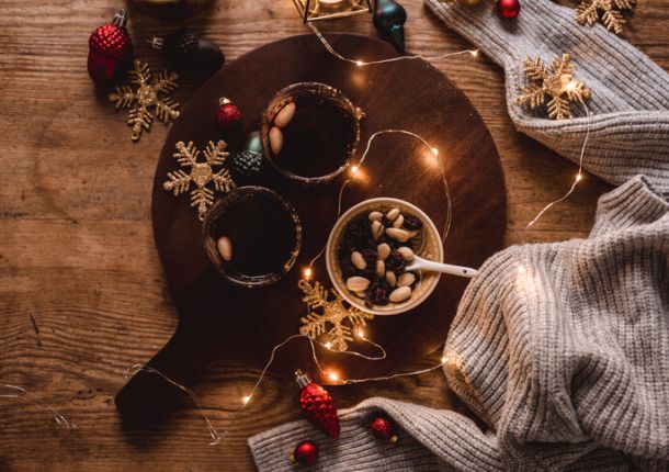 Auf einem Tisch stehen Glühwein, eine Schüssel mit Nüssen und Rosinen sowie eine kleine weihnachtliche Lichterkette.