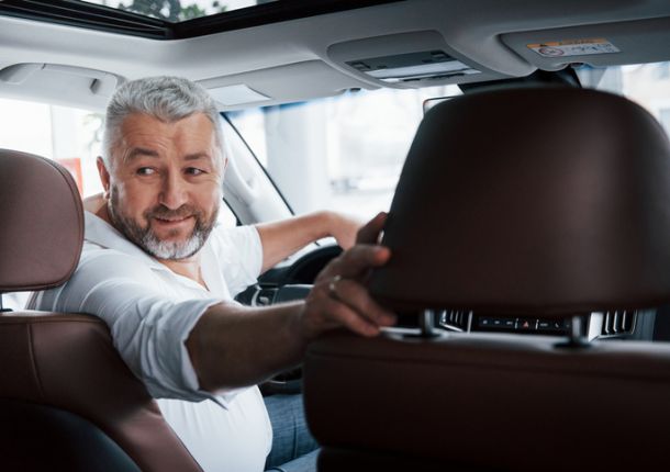 Ein älterer Mann fährt rückwärts mit einem Auto.