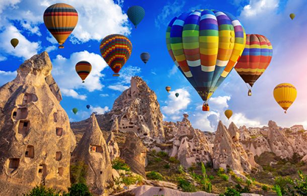 Mehrere bunte Heißluftballons steigen in den Himmel, umgeben von weißen Wolken und strahlendem Sonnenschein.