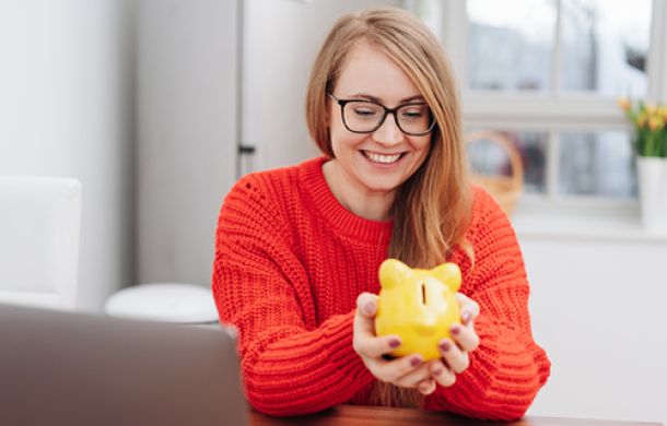 Eine blonde Frau mit einem Sparschwein in der Hand.
